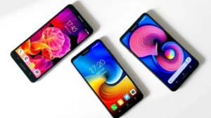 Flat lay of three mid-range smartphones arranged in a triangle on a clean white surface with subtle shadows, displaying different vibrant wallpapers on their screens showing off display quality