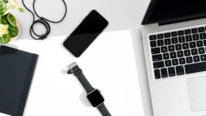 Overhead flatlay of modern tech gadgets: smartphone, wireless earbuds, smartwatch, and laptop arranged on minimalist desk with natural lighting