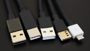 Close-up of various USB-C, Lightning, and Micro-USB cable connectors arranged side by side on a dark surface, showing connector details and differences